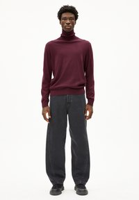 Bordeauxfarbener Rollkragenpullover aus weichem Material, kombiniert mit lockeren schwarzen Jeans mit glatter Textur und schwarzen Schuhen mit dicker Sohle.