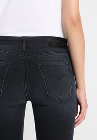 Musta denimpaita, jossa on istuva malli, puolikorkea vyötärökaitale, kaksi takataskua ja logopläkki vyötärökaitaleessa. Pehmeä rakenne.