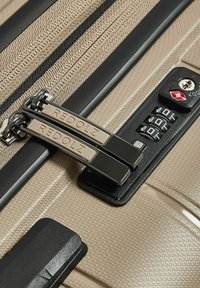 Valise beige texturée avec des tirettes zippées doubles portant l'étiquette "REDOLZ" et un verrou à combinaison TSA intégré réglé sur 000.