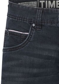 Dark denim jeans with a close-up view of the waistband, featuring a label and a contrasting pocket with decorative stitching and a small pocket.