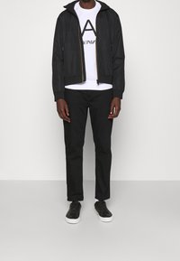 Svart zip-up jacka med huva, svart logotyp t-shirt och svarta byxor. Texturerad tyg, avslappnad design, kombinerat med svarta sneakers.