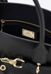 Borsa a tracolla in pelle nera con hardware dorato, dotata di chiusura con zip e una placca con il marchio all'interno che recita "WITTCIHEN, FATTO A MANO IN ITALIA, PELLE PREGIATA."