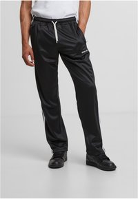 Crne atletske hlače od glatkog materijala, s pojasom na vezanje, bijelim bočnim prugama i malim logom na bedru.