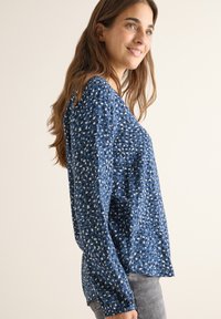 Chemise à manches longues bleu à motifs, offrant une coupe ample avec des formes variées en blanc et bleu clair, fabriquée à partir d'un tissu doux.