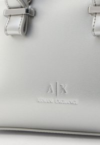 Sac à main en simili cuir argenté avec une texture lisse, des accents en métal argenté, et le logo embossé "A|X ARMANI EXCHANGE". Détail de nœud amovible.