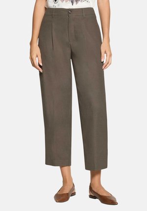 Donna che indossa pantaloni marroni a vita alta, a gamba larga e corta, con chiusura a bottone e cerniera, e ballerine marroni con punta appuntita.