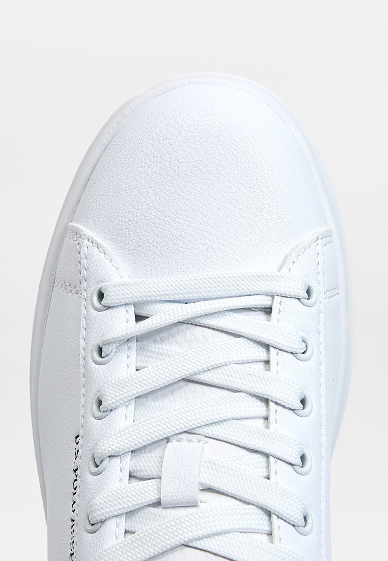 Zapatilla blanca de cuero con textura suave, punta redonda y cordones planos. Presenta una marca en el costado y un diseño minimalista.