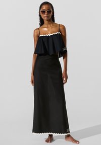 Sort todelt sæt bestående af en vid udsvinget cropped top med bølgede kanter og et langt skørt med matchende bølget kant. Solbriller fuldender looket.