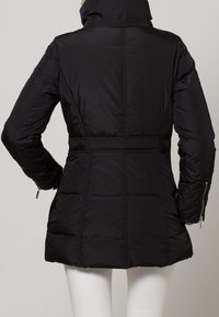 Giacca puffa nera con colletto alto, vita aderente e design trapuntato. Presenta tasche laterali con zip e un esterno liscio e resistente all'acqua.