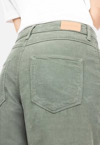 Olivgrüne Cordhosen mit strukturierter Oberfläche, ausgestattet mit Gesäßtaschen und einem Lederetikett am Bund, welches den Markennamen zeigt.