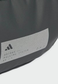 Borsa per il sistema di imballaggio nera con superficie testurizzata, con etichetta grigia su cui è stampato testo e logo neri; i dettagli includono "ADIDAS" e "KF 24."