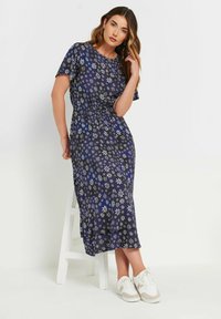 Marinblå blommig maxiklänning med korta ärmar, elastisk midja, lätt tyg och vita blomster mönster. Matchad med vita sneakers.