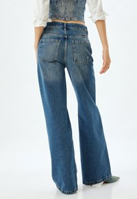 Jeans de mezclilla de pierna ancha en azul, con cintura alta, bolsillos traseros y un acabado deslavado con dobladillos limpios.