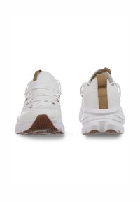 Zapatillas deportivas blancas con un upper texturizado, cordones elásticos y una lengüeta de acento marrón. Presenta una suela gruesa con un agarre estampado.