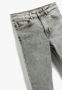 Jeans de mezclilla gris deslavado con corte slim, cinco bolsillos y detalles de costura naranja a lo largo de las costuras y la cinturilla.