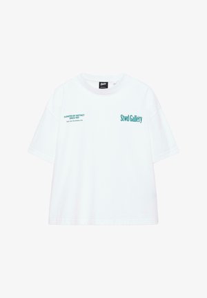 Valkoinen lyhythihainen T-paita, jossa turkoosi teksti "Stwd Gallery" oikealla rinnalla ja "Curated by Instinct Since 1991" vasemmalla rinnalla.