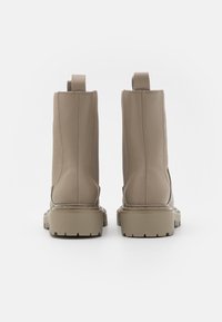 Bottes de cheville en cuir beige avec une finition texturée, des panneaux élastiques sur les côtés et une semelle en caoutchouc épaisse. Équipées de languettes pour un enfilage facile.