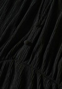 Tissu noir froissé avec deux boutons recouverts et un détail de couture plissée près du bas du cadre.