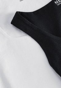Czarno-białe bluzki nachodzące na siebie, wykonane z miękkiego bawełnianego materiału, z okrągłym dekoltem i szerokimi ramiączkami na czarnej bluzce. Brak wzorów lub akcentów.