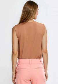 Brązowy top bez rękawów w połączeniu z różowymi, dopasowanymi spodniami o gładkiej teksturze i przylegającym kroju, z plisami z tyłu i prostym pasem.