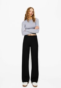 Pantalons larges noirs en tissu lisse, dotés d'une fermeture à un bouton. Associés à un haut court à manches longues gris clair.