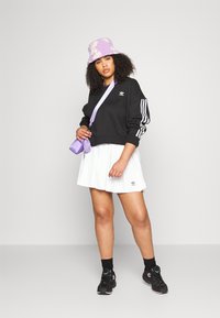 Melna apgriezta sporta krekla ar baltām svītrām, balta plisēta svārku, purpura krāsas ķivere ar ziedu rakstu, purpura krāsas soma un melnas kedas.