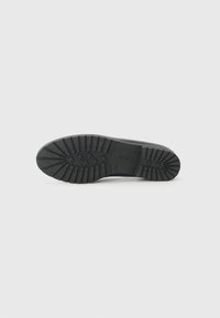 Semelle de chaussure en caoutchouc noir avec un motif de traction texturé pour une meilleure adhérence, dotée de rainures prononcées et d'une construction robuste.