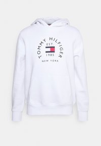 Sudadera blanca hecha de una mezcla de algodón, que cuenta con un bolsillo frontal, capucha con cordones y un logo circular con acentos en rojo, azul y negro.