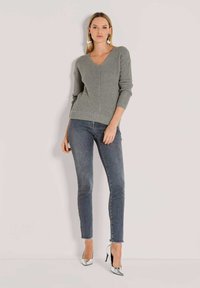 Grauer gestrickter Pullover mit V-Ausschnitt, gerippter Textur und Dreiviertelärmeln, kombiniert mit dunkelblauen Skinny-Jeans und silbernen High Heels.
