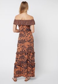 Maxi-jurk in oranje met zwart bloemenpatroon, off-the-shoulder ontwerp, geruisde mouwen en gelaagde rok. Gestructureerde stof. Platte sandalen.