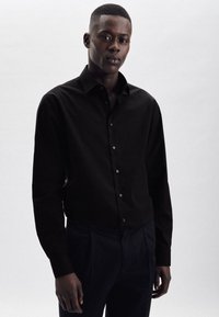 Zwarte longsleeve shirt met knopen, zachte textuur, getailleerde pasvorm, klassieke kraag, gedragen met donkere broek. Eenvoudig ontwerp, zonder patronen.