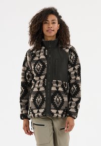 Veste en polaire avec un motif géométrique noir et beige, présentant une poche et un col noirs unis. Fermeture éclair, coupe décontractée, tissu texturé.