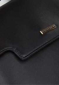 Borsa in pelle nera con superficie texturizzata, dotata di una placca loghi in metallo dorato e di un risvolto curvo. I bordi cuciti migliorano il design.