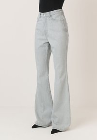 Šviesiai pilkos plačios džinsinės kelnės su aukštu liemeniu, užsegimu mygtuku ir užtrauktuku, bei penkių kišenių dizainu. Pagamintos iš lygaus džinsinio audinio.