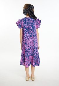 Mėlynos ir rožinės leopardų rašto suknele su suglebusiais rankovėmis, sluoksniuota sijonu ir užpakaline kaspino detale. Dėvima su auksinės spalvos bateliais.