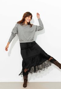 Sweat-shirt gris à col rond, associé à une jupe longue noire avec bordure en dentelle et plis évasés. Bottines marron complètent le look.