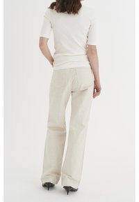 Ljusbeige ribbad topp med korta ärmar som är kombinerad med ljusbeiga vida byxor. Byxorna har bakfickor och en lätt textur. Svarta klackar syns.