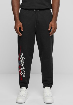 Svarte joggebukser med snor i livet, med hvit og rød "Brooklyn"-skrift og et blått stjernedesign på venstre ben. Sammen med hvite joggesko.