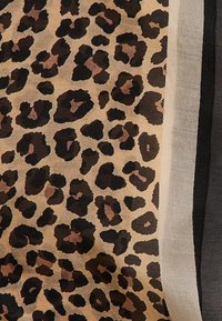 Écharpe à imprimé léopard avec un fond beige, ornée de taches noires et brunes, bordée de contours beige et gris foncé. Tissu doux et texturé.