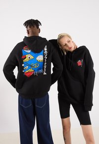 Black hoodies, one features colorful food graphics on the back, the other has a small red and white logo on the chest. Cotton material.