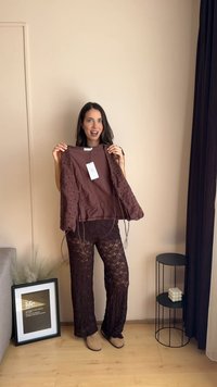 Cardigan all'uncinetto marrone con fronte annodato, indossato sopra pantaloni in pizzo abbinati. L'outfit presenta una consistenza morbida e intricate fantasie in pizzo.