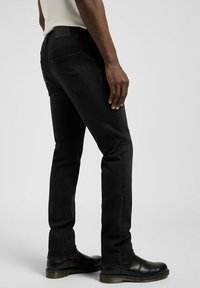 Czarne jeansy z denimu o dopasowanym fasonie i prostych nogawkach. Pas na talii ozdobiony jest naszywką z logo, a faktura tkaniny jest gładka.