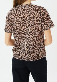 Tričko s krátkým rukávem, růžový leopardí vzor, kulatý výstřih a volný střih. Tkanina vypadá měkce a hladce na dotek. Černé džíny z denimu.