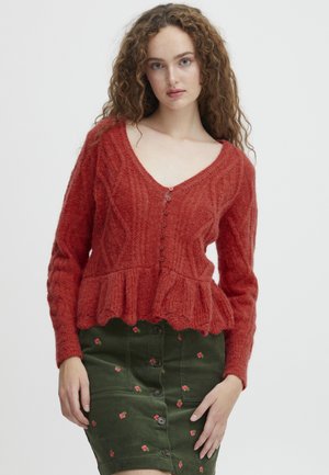 Rød strikket cardigan med V-hals, der har en peplum-krave, kabelstrik mønstre og knaplukning. Sæt sammen med en grøn blomsterkjole.