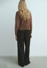 Brązowy krótki sweter o fakturowanym wykończeniu, zestawiony z czarnymi spodniami o szerokich nogawkach z wysokim stanem. Tylny widok ukazuje luźny krój i sylwetkę.