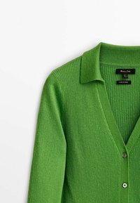 Grön ribbad stickad cardigan med krage och knappstängning, märkt storlek small, tillverkad i Kina, uppställd på vit bakgrund.