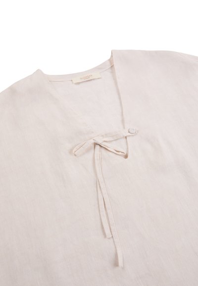 Beżowy lniany top z dekoltem w serek i zawiązywanym z przodu wiązaniem z tkaniny, o miękkiej fakturze i minimalistycznym designie.