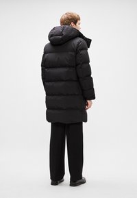 Black puffer coat with a hood, featuring a quilted design and polyester material. Long hem and slightly loose fit create a modern silhouette.