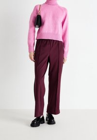 Rosa stickad tröja med ribbad polo, parat med vinröda vida byxor med sidoslitsar och svarta kraftiga skor.