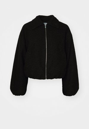 Svart cropped jakke i et mykt, strukturert stoff. Har krage og lange, litt puffete ermer med glidelås foran.